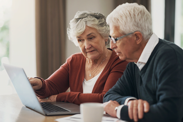 Older couple planning their retirement together using laptop and documents