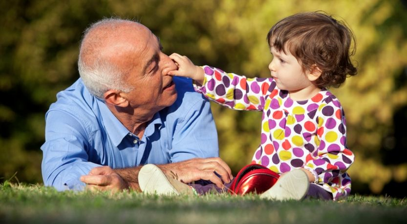 Grandfather playing with young grandchild on grass outdoors