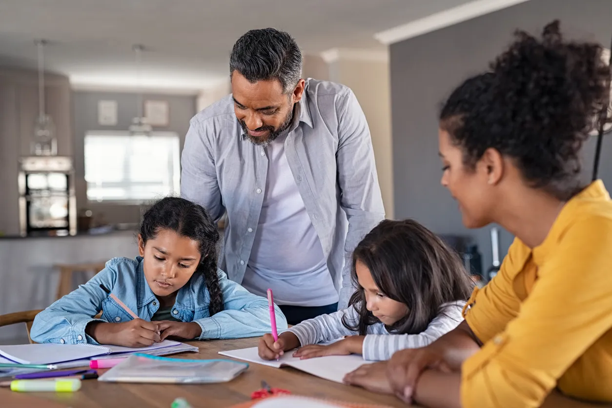 Parents helping their children with homework at the kitchen table